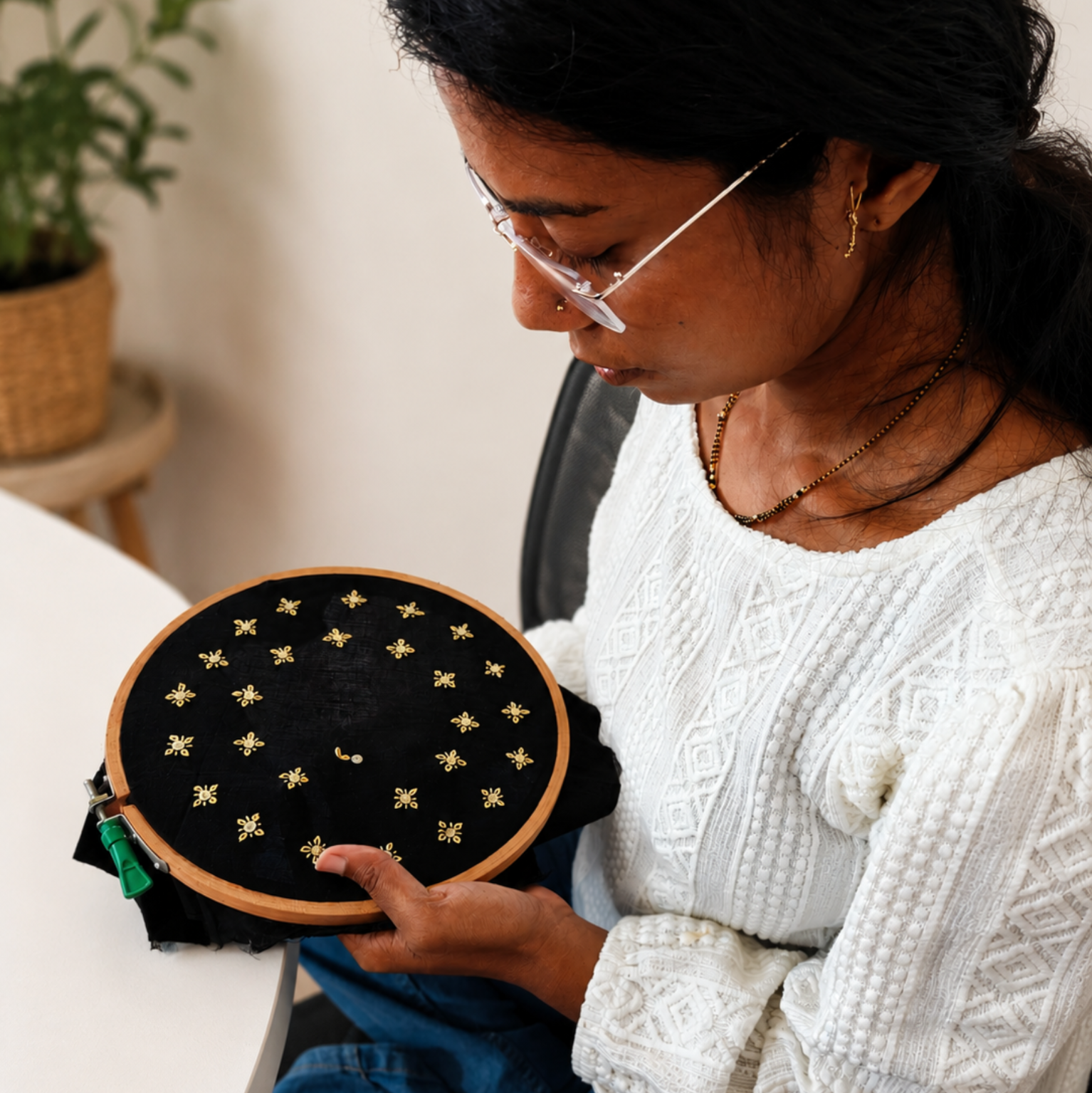 Person holding a embroidery hoop with black fabric and gold thread in a home setting.
